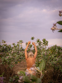 Rear view of sensuous naked woman standing by plants against sky