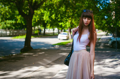 Young woman standing on sidewalk against trees