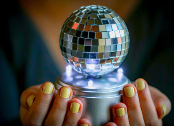 Hands with yellow nail polish holding a shiny disco ball