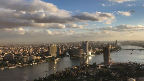 High angle view of buildings by river against cloudy sky