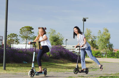 Happy family lifestyle. mother, boy, girl walking in city. ride scooters. laughing on summer. fun