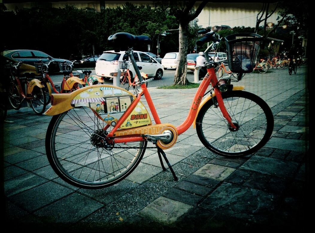 bicycle, transportation, mode of transport, land vehicle, parked, stationary, parking, street, parking lot, motorcycle, travel, car, cycle, road, outdoors, day, riding, sidewalk, cycling, shadow