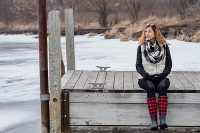 Thoughtful woman sitting on pier over frozen lake