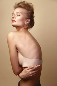 Portrait of young woman in bra against brown background