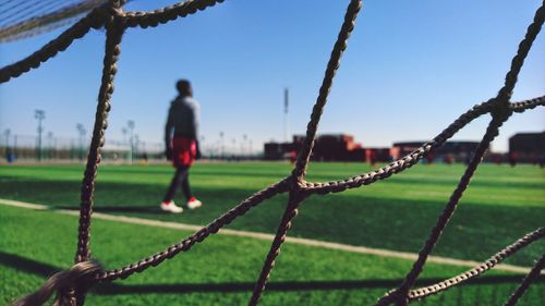 Man seen through fence walking on field against sky