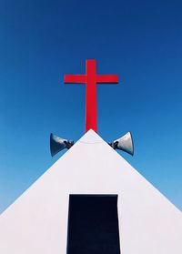 Low angle view of cross against building against clear blue sky