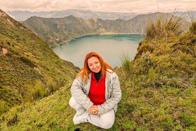 Portrait of smiling young woman standing on mountain against sky