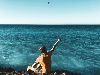 Rear view of man sitting on sea against clear sky