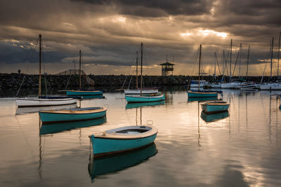 Boats moored in harbor at sunset