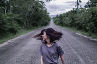 Woman tossing hair while standing on road amidst trees