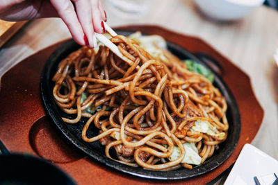 Close-up of hand holding noodles in plate on table
