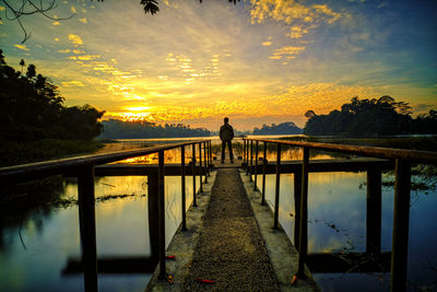 Man standing by railing against sky during sunset