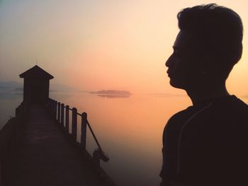 Young man standing on pier over lake against sky during sunset