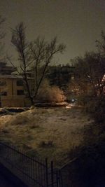 Bare trees and buildings against sky at dusk