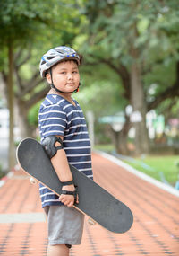 Portrait of boy holding skateboard in park