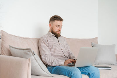 Young attractive, smiling bearded guy browsing his laptop while sitting at home