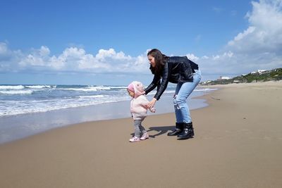 Mother and daughter at beach against blue sky