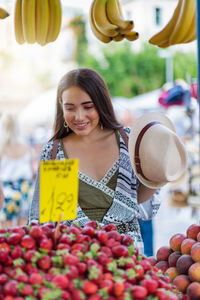 Smiling young woman buying fruits at market stall