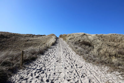 Surface level of dirt road against clear blue sky