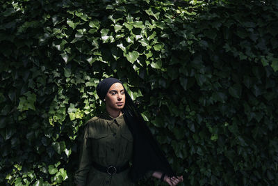 Portrait of young woman standing against plants