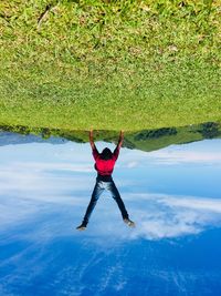 Upside down image of man doing handstand on field against blue sky