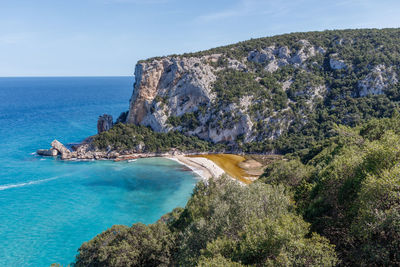 A cala luna beach in sardinia east coast with wooded hills and a sandy beach.