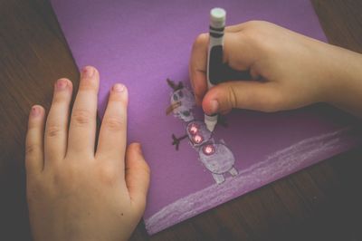 Cropped image of hands drawing on purple paper