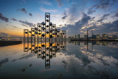 Reflection of buildings in city against sky during sunset