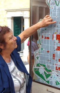 Profile of an old lady consulting a touristic map and pointing on a destination