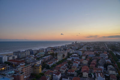 High angle view of buildings and sea against sky at sunset