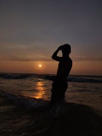 Silhouette man standing on beach against sky during sunset