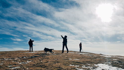 Silhouette people and dog playing on field against sky during winter