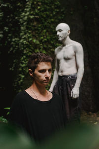 Young man looking away while standing on tree in forest