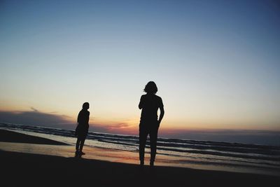 Silhouette people on beach against clear sky during sunset