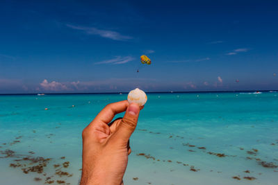 Close-up of hand holding sea against blue sky