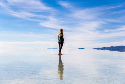 Rear view of young woman standing by infinity pool against cloudy sky