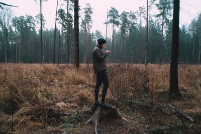 Man using mobile phone while standing on tree stump in forest