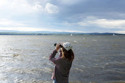 Rear view of young woman standing at sea against sky