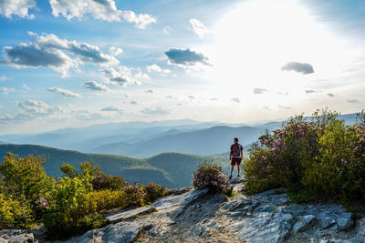 Rear view of male hiker standing on cliff against mountains