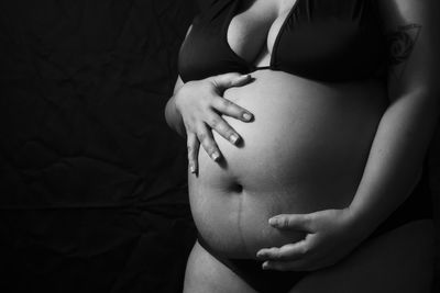 Midsection of woman touching face against black background