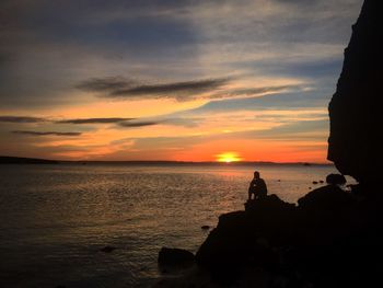 Silhouette of person sitting on rock at beach