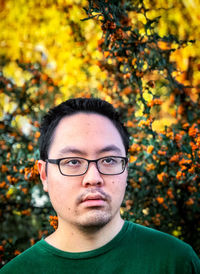 Portrait of young man wearing eyeglasses against orange rowan berries and trees at sunset.