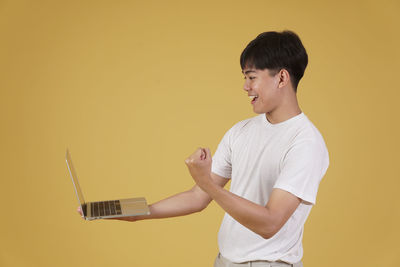 Young man using smart phone against yellow background