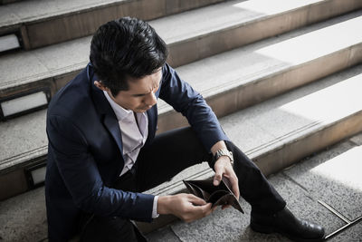 Businessman holding wallet while sitting on steps