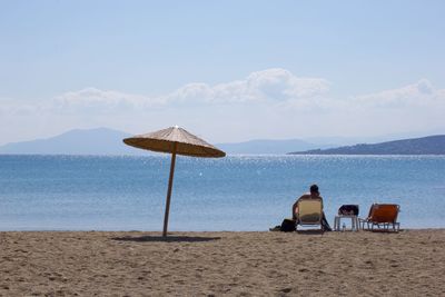 Rear view of woman sitting on beach against sky