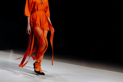 Trendy women's look orange tights and designer shorts, fashion model walking on the podium