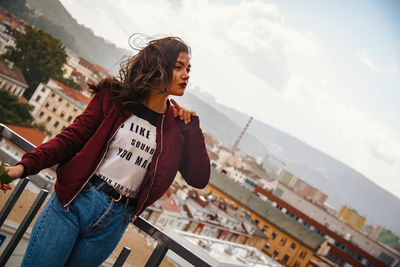 Side view of woman standing by cityscape against sky