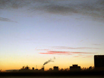 Silhouette of factory against sky at sunset