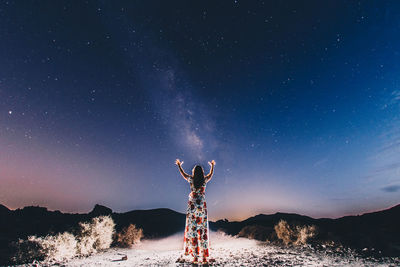 Rear view of woman standing against sky at night