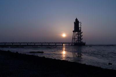 Silhouette lighthouse by sea against sky during sunset